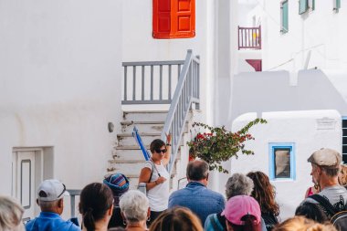 Mykonos Town, Yunanistan - 23 Eylül 2019: Adaların iyi korunmuş liman ve başkenti Hora 'da (ayrıca Mykonos Town olarak da bilinir) bir sokakta bir grup turistle konuşan tur rehberi. Seçici odak.