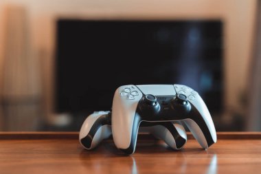 Londra, İngiltere - 25 Mayıs 2021: Masada iki Playstation 5 (PS5) denetleyicisi, arka planda televizyon, seçici odak. Playstation 5, Sony 'nin Kasım 2020' de piyasaya sürdüğü video oyunu konsolu..