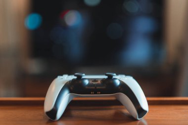 Londra, İngiltere - 25 Mayıs 2021: Masada bir beyaz Playstation 5 (PS5) denetleyici, arka planda televizyon, seçici odak. Playstation 5, Sony 'nin Kasım 2020' de piyasaya sürdüğü son video oyunu konsoludur.