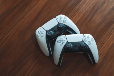 Londra, İngiltere - 25 Mayıs 2021: Tahta bir sehpanın üzerindeki Playstation 5 (PS5) kontrolörleri. Playstation 5, Sony 'nin Kasım 2020' de piyasaya sürdüğü son video oyunu konsoludur..