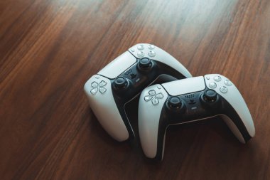 Londra, İngiltere - 25 Mayıs 2021: Tahta bir masadaki iki Playstation 5 (PS5) kontrolörünü kapatın. Playstation 5, Sony 'nin Kasım 2020' de piyasaya sürdüğü son video oyunu konsolu..