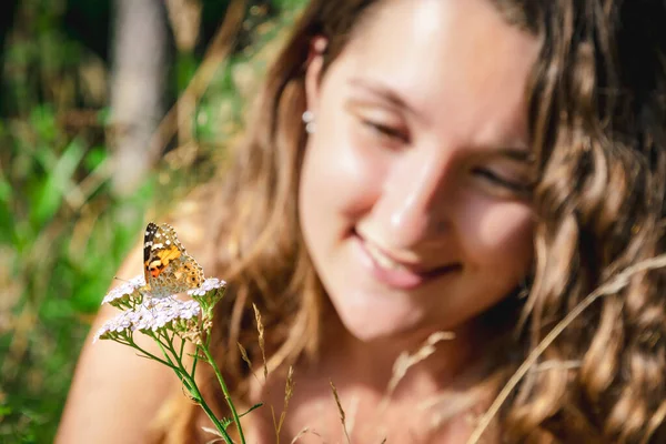 Young woman looking at a painted lady butterfly on a flower