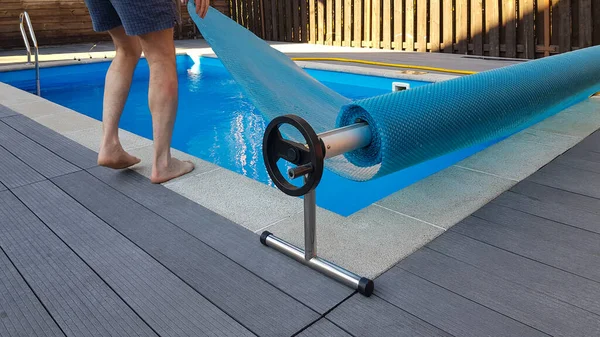 Man covers swimming pool with cover for protection against dirt, leaves, heating and cooling water.