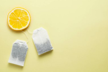 Çay poşetleri ve sarı arka planda bir dilim limon.