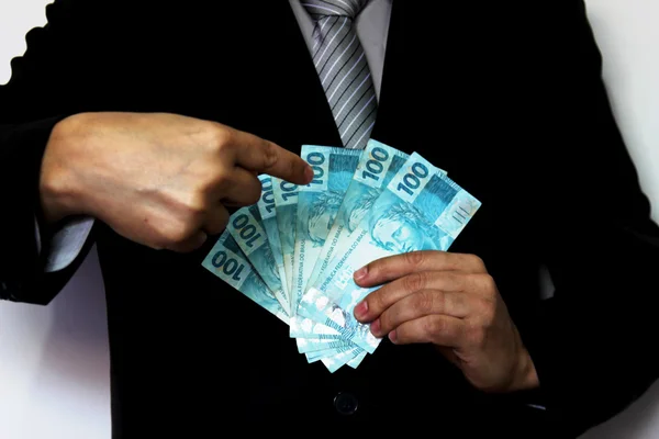 Suited man holding Brazilian bank notes and pointing with his finger — Stock Photo, Image