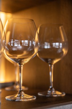 Ahşap bir rafta temiz, boş şarap kadehlerini yakın çekim. Lüks bir restoran içinde sıcak ortam aydınlatması..