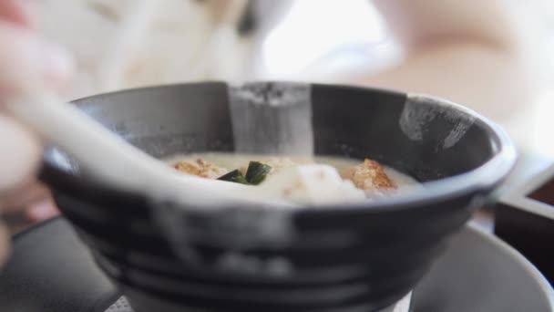 Une femme mange une cuillerée d'une soupe de noix de coco asiatique avec du tofu et du poisson. — Video