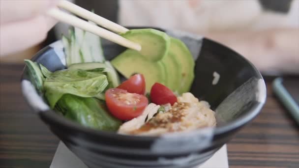 En gourmetflicka på en asiatisk restaurang äter en skål med avokado, tomater, ris, spenat och kyckling. — Stockvideo