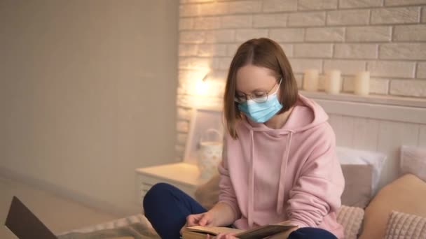 Elegante estudiante chica en una máscara médica y gafas enfermo covid-19 lee un libro. — Vídeos de Stock