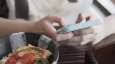 Kız Asya restoranında yemek yerken akıllı telefon kullanıyor..
