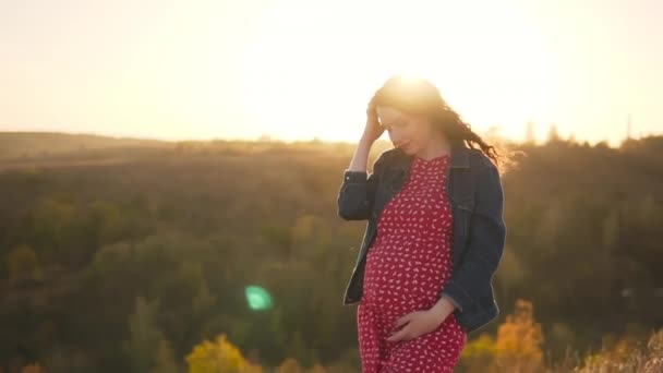 Gravidanza felice: una giovane ragazza incinta sorride e raddrizza i capelli svolazzando nel vento. — Video Stock