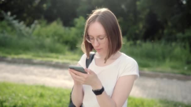 Giovane ragazza attraente in occhiali con un orologio intelligente sulla mano facendo shopping online con uno smartphone. — Video Stock