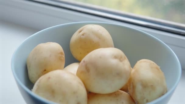 在白色窗台上用深蓝色的碗洗开胃土豆. — 图库视频影像