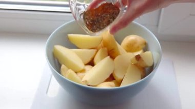 Bir ev hanımı, baharat kokulu kibir ile kırsal bir şekilde pişirmek için patates dilimleri serpiyor.. 