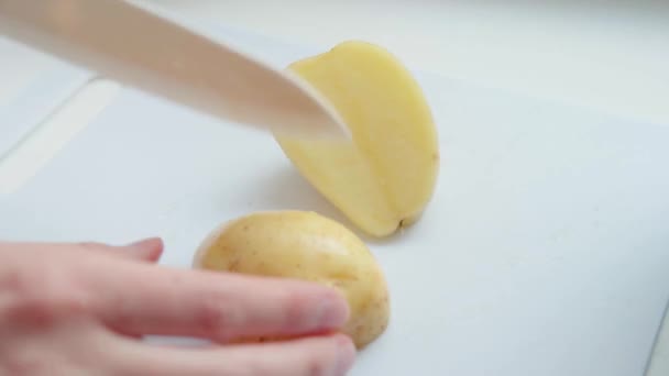 De chef snijdt de jonge aardappelen in plakjes op een beige keukenbord close-up. — Stockvideo