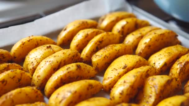 Los trozos del pueblo-estilo o las patatas griegas en el aceite de oliva y las hierbas sobre el pergamino. — Vídeos de Stock