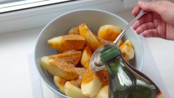 Seorang wanita menambahkan minyak zaitun sayuran ke dalam mangkuk irisan kentang. Memasak kentang Yunani. — Stok Video