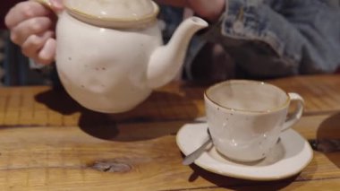 Kot ceketli ve pembe kapüşonlu bir kız çayını seramik çay bardağına dolduruyor..