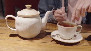 Kot ceketli sıradan bir kız bir bardak çaya şeker döker..