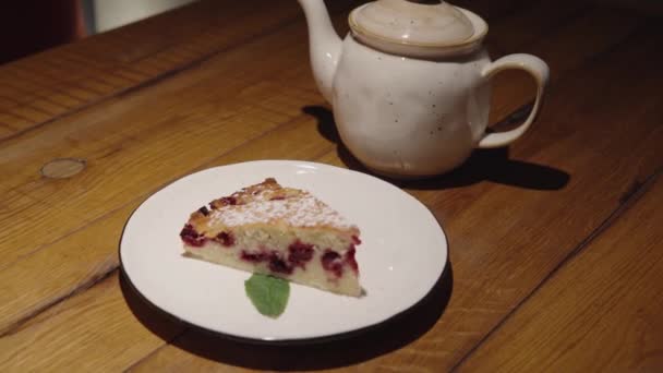 Pastel de cereza con menta y decoración de azúcar en polvo en un plato cerca de la tetera se encuentra en la mesa. — Vídeo de stock