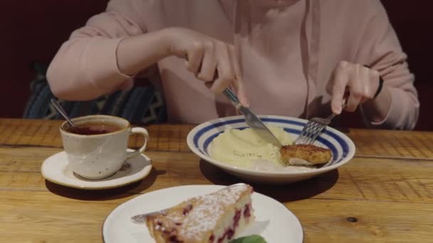 Uma menina em um hoodie rosa janta em um restaurante, come costeleta de frango e purê de batatas. — Vídeo de Stock