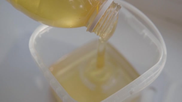 Il miele di acacia trasparente liquido di alta qualità scorre dalla bottiglia in contenitori di plastica prodotti in un apiario domestico. — Video Stock