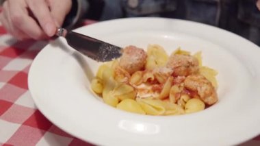 Bir kadın domates soslu tavuk filetosundan yapılmış makarna ve köfte yer..