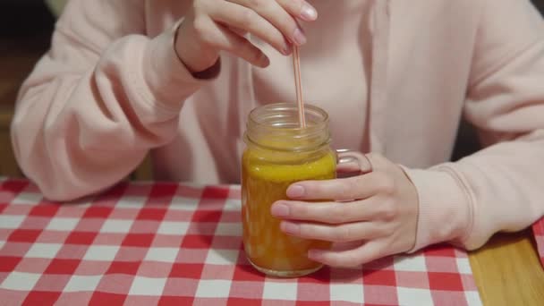 La fille boit du thé vitaminé à l'argousier chaud à travers une paille de tasse en verre. — Video