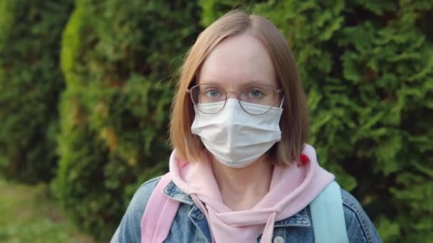 Retrato de una niña en una máscara protectora, gafas y chaqueta de mezclilla al aire libre. — Vídeo de stock