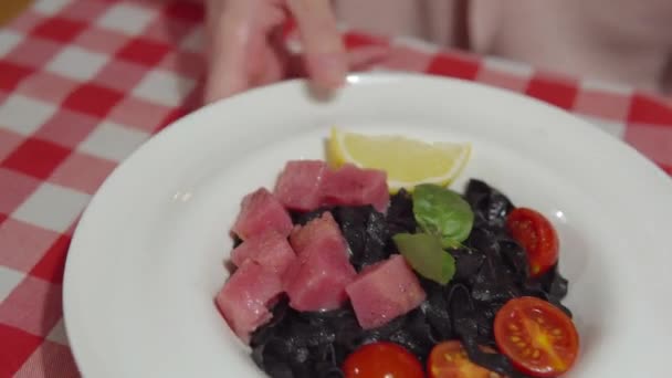 Händer av en ung kvinna visar svart pasta med bläckfisk bläck med rå tonfisk, tomater, basilika och sås. — Stockvideo
