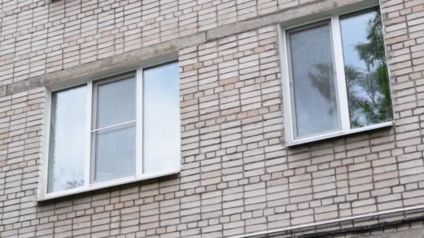 Cerrar dos ventanas acristaladas del edificio residencial de la Unión Soviética. Edificio residencial exterior con fondo de cielo gris. fachada de ladrillo. Edificio cuenta con pared verde exterior y pequeños balcones — Vídeos de Stock