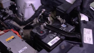 Eldivenlerle adamın elini kapat ve elektrikli bir arabanın aküsünü işaret et. Profesyonel tamirci tamirhanedeki motoru kontrol ediyor ve kaputun altındaki bozuk detayları gösteren müşteriyi dinliyor.