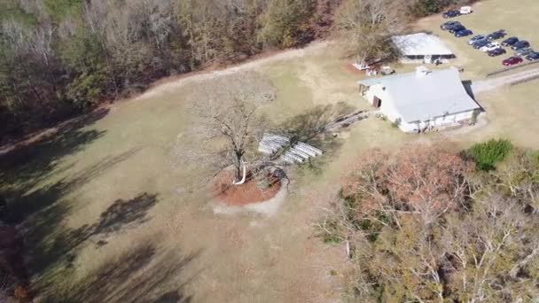 Drone câmera lenta um belo lugar para um casamento sob uma árvore com fileiras brancas de cadeiras e uma igreja solitária. de um casal de casamentos sob árvores, cercado por flores e grama. Tiro aéreo — Vídeo de Stock