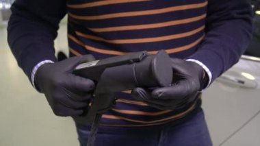 Araba galerisinde siyah lastik eldiven giyen bir adam elektrikli araçlar için yüksek voltajlı bir kablo gösteriyor. Elektrikli araba şarjı. EV arabası. Eko enerji, ulaşım ve güç kaynağı 4K