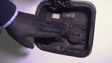 Siyah lastik eldivenli bir adam elektrikli bir arabanın şarj olan prizini gösterir ve kablo kontaklarını koruyan kapağı eline bastırarak açar. Eko enerji ve güç kaynağı 4K