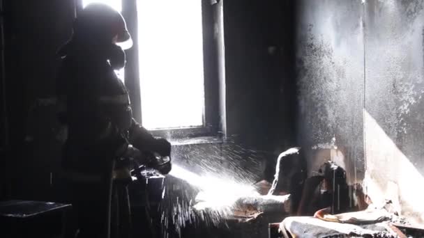 Пожарный выбрасывает горящую мебель в комнату в квартире у Огненной Костры. Тушение лесного пожара. Костер. Много дыма, пар от огня потушен. Пожарный распыляет воду и пену из шланга — стоковое видео