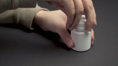 Bir kadının eli kapanıyor ve siyah sağlık masasındaki haplarla dolu şişeyi açıyor. Şişe mühürlendi. İlaç alan biri. Acıyı dindir. Sağlık ve ilaç kavramı 4k