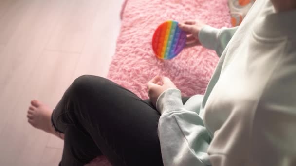 Mãos de uma menina sentada no sofá jogar em colorido popit brinquedo anti-stress para crianças e adultos, o desenvolvimento de habilidades motoras finas das mãos. Brinquedo popular na moda pop-lo. Toque nas bolhas 4k — Vídeo de Stock