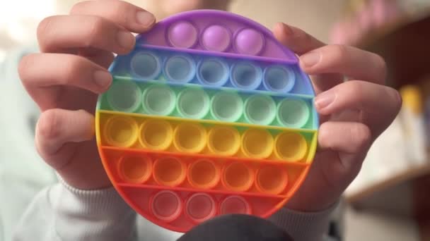 Les mains d'une fille assise sur le canapé jouent dans le popit jouet anti-stress coloré pour les enfants et les adultes, le développement de la motricité fine des mains. Tendance populaire jouet pop it. Appuyez sur les bulles 4k — Video