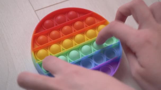 Le mani di una ragazza seduta sul divano giocano in colorato popit giocattolo anti-stress per bambini e adulti, lo sviluppo di abilità motorie fini delle mani. Trendy giocattolo popolare pop it. Toccare le bolle 4k — Video Stock