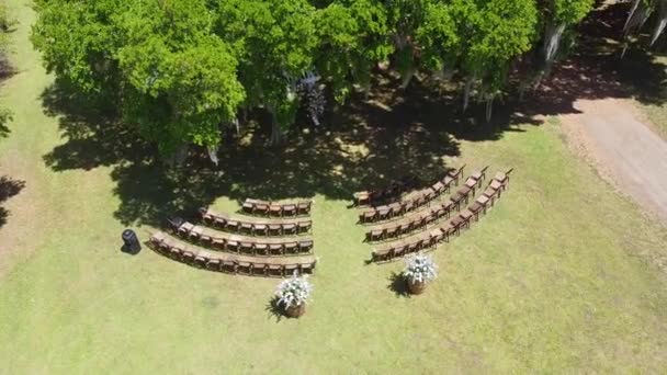 Vue de dessus du lieu de mariage dans un champ verdoyant et une maison dans le village près de la forêt et de la mer. Tradition de cérémonie de mariage avec décor décoré sur pelouse. De belles fleurs. Rangées de chaises blanches 4k — Video