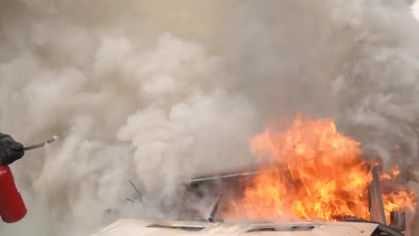 Bomberos profesionales que ayudan a extinguir con un extintor de incendios coche roto después de un accidente de tráfico en el campo. Un montón de llamas y humo salen del coche. Bomberos salvan a la gente en cámara lenta — Vídeo de stock