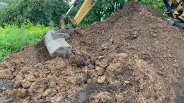 Bir kazıcı temel inşa etmek için kil toprağı bir temel çukuruna gömer. Toprağı, geçmişi, endüstrisi olan kazıcı demir kovası. Kazıcı, kablo döşemek için bir siper kazıyor.