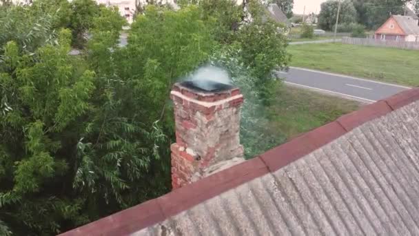 Vista aérea A fumaça branca da lareira sobe acima da chaminé de tijolo na casa residencial com árvores verdes no fundo, estática. telhado de ardósia cinza e fumaça de chaminés da antiga casa tradicional — Vídeo de Stock