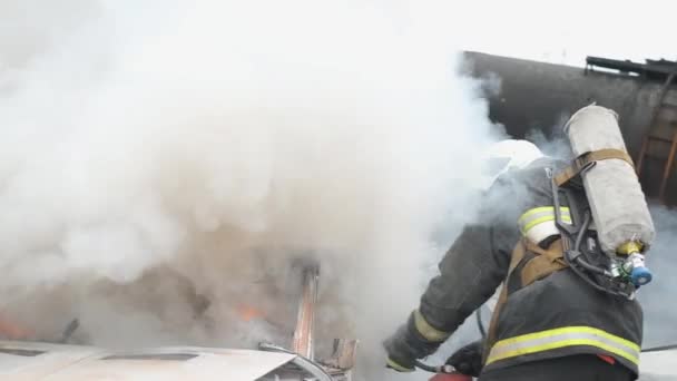 En la escena del accidente de tráfico: Un trabajador de rescate de incendios extingue profesionalmente un incendio en un automóvil con un extintor de incendios. Mucho fuego y humo. Desbloqueo de víctimas. Servicios de primeros auxilios — Vídeos de Stock