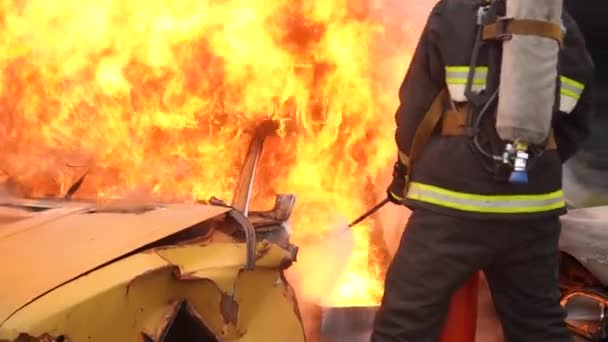 En la escena del accidente de tráfico: Un trabajador de rescate de incendios extingue profesionalmente un incendio en un automóvil con un extintor de incendios. Mucho fuego y humo. Desbloqueo de víctimas. Servicios de primeros auxilios — Vídeos de Stock