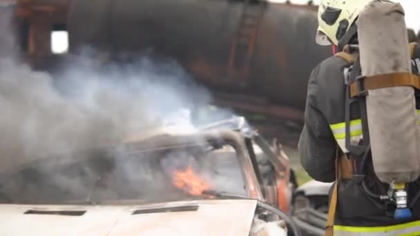 En la escena del accidente de tráfico: Un trabajador de rescate de incendios extingue profesionalmente un incendio en un automóvil con un extintor de incendios. Mucho fuego y humo. Desbloqueo de víctimas. Servicios de primeros auxilios — Vídeos de Stock