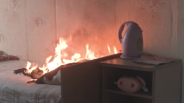 El dormitorio está en llamas con mucho humo. La cama, la mesita de noche, la tetera de plástico, el papel pintado y las estanterías están en llamas en una casa residencial. Fotografía cinematográfica de las secuelas de un incendio de dos alarmas 4k — Vídeo de stock