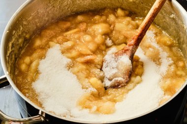 Şeker eklemek ve ahşap kaşıkla dürtmek ev yapımı elma reçelini pişirme kabına hazırlamak