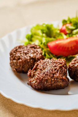 Lezzetli kıymalı biftek, çıplak hamburger ve beyaz tabakta sebze salatası.
